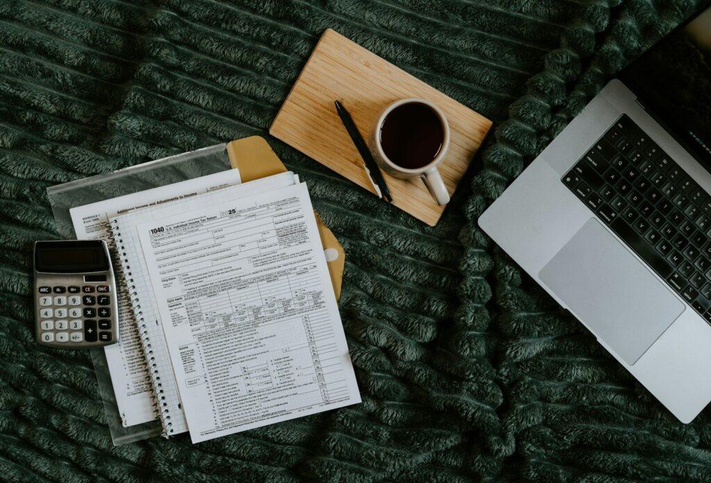Laptop, papers, calculator, and coffee on blanket.